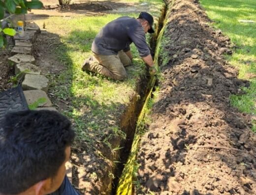 Three Allied Foundation workers installing BioBarrier root barrier fabric in a trench beside a lawn